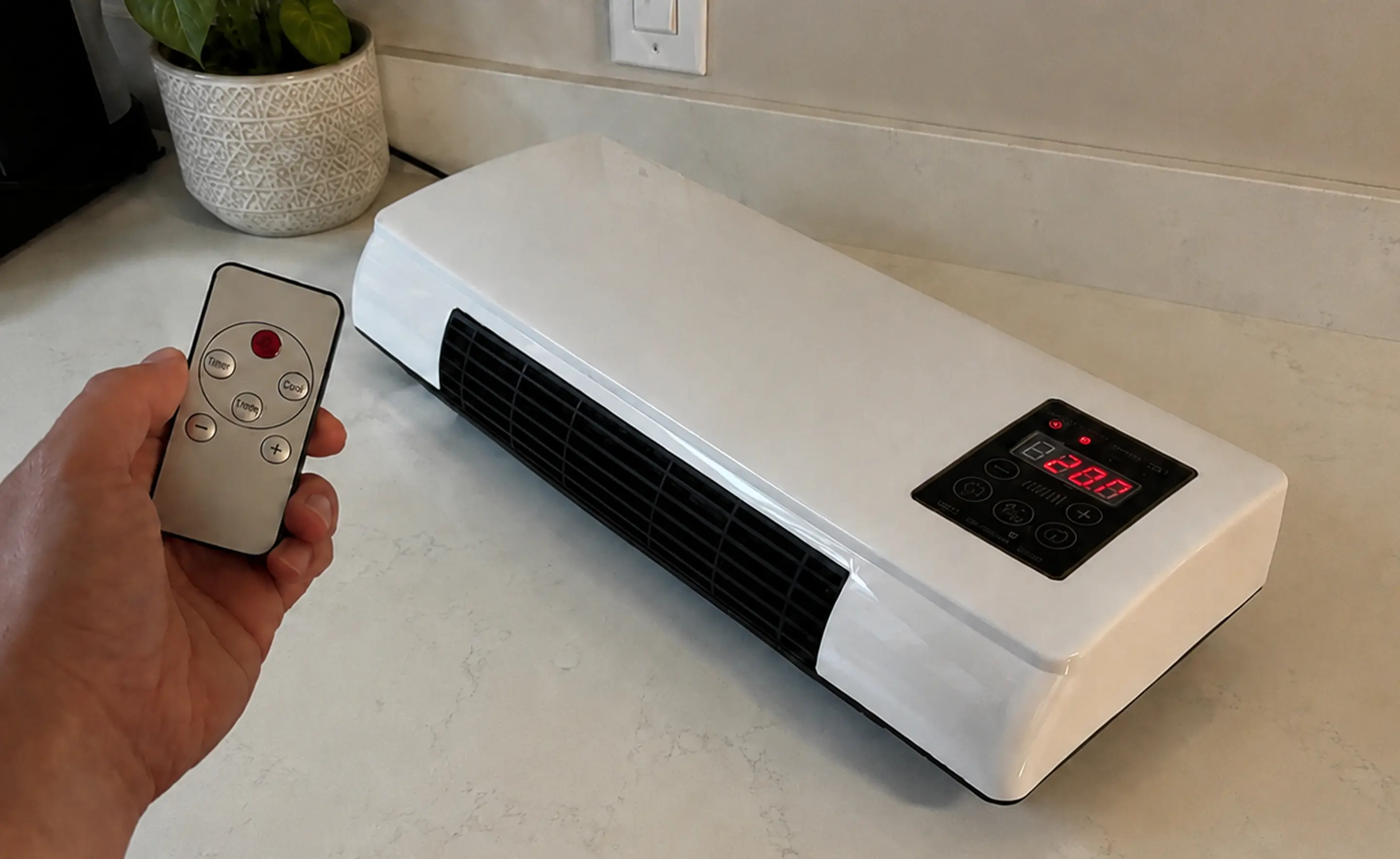 A hand holding the CoolCove remote beside the unit and its lit display